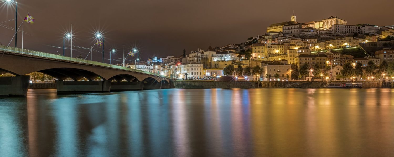 A bridge on the sea in Coimbra with the lights reflecting on the water during the night in Portugal